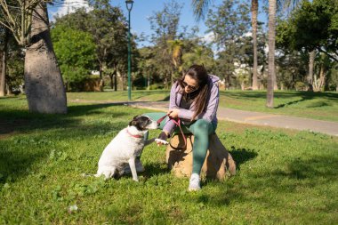 Ağaç kütüğünde oturan bir kadın, köpeğine parkta patisini sallamayı öğretiyor.