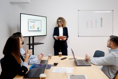 Modern bir ofis toplantısında iş arkadaşlarına veri sunan iş kadını