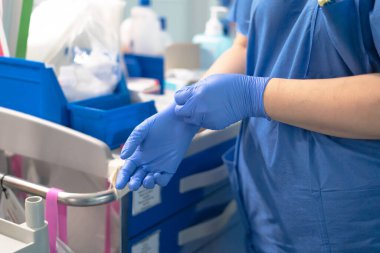 Sağlık çalışanı tıbbi prosedüre hazırlanıyor, koruyucu mavi eldivenler giyiyor.