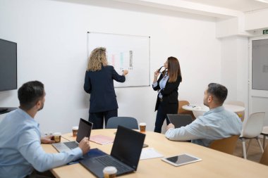 İş yöneticisi, konferans odasındaki meslektaşlarına verileri beyaz tahtayla sunuyor.