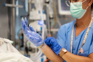 Hemşire tıbbi eldiven takıyor, hastane koğuşunda prosedüre hazırlanıyor.