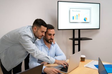 İki erkek profesyonel iş stratejisini tartışırken bir dizüstü bilgisayar ve ekranda sonuçları analiz ediyorlar.