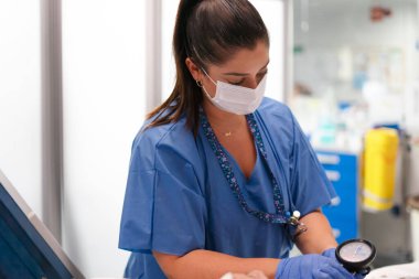 Hemşire koruyucu bir maske takıyor ve hastanın tansiyonunu ölçüyor.