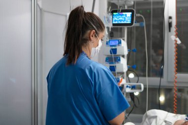 Hastane yoğun bakım ünitesindeki hastalarla ilgilenen hemşire, tıbbi ekipmanları izliyor.