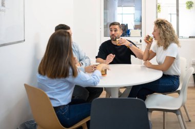 İş arkadaşları yuvarlak bir masada kahve içerken gündelik bir tartışma yapıyorlar.