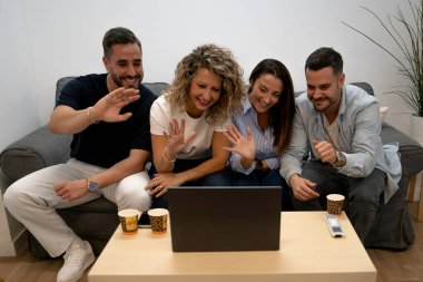 Bir grup arkadaş evdeki dizüstü bilgisayarda el sallıyor.