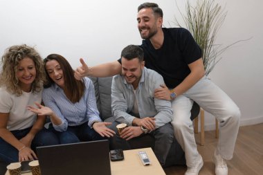 Dizüstü bilgisayarı izleyen ve zaferi kutlayan bir grup mutlu genç arkadaş.