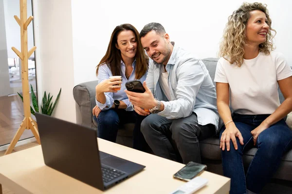 Üç gülümseyen meslektaş bir kanepede oturup, bir telefon molası sırasında bir anı paylaşıyorlar.