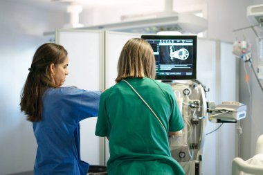 Klinik ortamda modern bir hemodiyaliz makinesi üzerinde çalışan tıp uzmanları