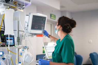 Hastane yoğun bakımında tıbbi solunum cihazı ve hasta izleme cihazı kullanan hemşire.