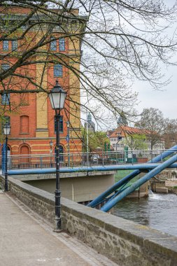 Arka planda bina olan bir nehir üzerinde köprü. Köprü mavi ve bina kırmızı.