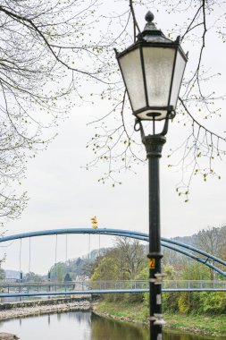 Kamen, Almanya 'da bir sokak lambası direği, arkasında mavi bir metal köprü ve bir fare heykeli bulunan bir nehir kıyısında yer alıyor. Fotoğraf bulutlu bir havada çekildi..