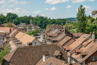 İsviçre 'de birçok evi ve kilisesi olan bir Bern şehri manzarası. Evlerin hepsi farklı boyutlarda ve çatıları farklı. Gökyüzü mavi ve bazı bulutlar var.
