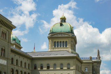 Bern İsviçre 'nin tepesinde yeşil kubbesi olan büyük bir bina. Kubbe, üzerinde kırmızı bayrak olan bir binanın tepesinde. Bina bulutlu bir gökyüzü ile çevrilidir.