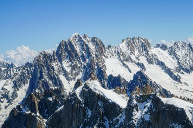 Dağlar karla kaplı ve gökyüzü açık ve mavi. Manzara huzurlu ve sakin, dağlar manzaranın üzerinde yükseliyor.