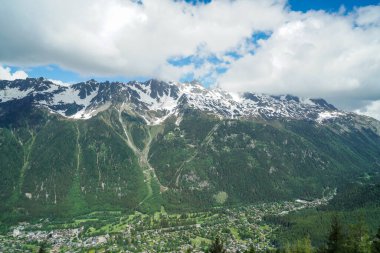 Aşağıdaki Alp Dağları 'nın manzarası vadide Fransa' nın Chamonix kasabasını görebiliriz. Gökyüzü bulutlu. Dağlar yeşil ve karla kaplı..