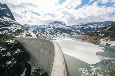 Finhaut İsviçre Alplerinde büyük bir beton baraj Tyrolienne Emossionnelle. Suda buz var. Arka planda karla kaplı dağlar görünüyor.