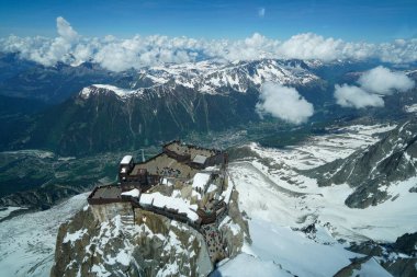 Tepesi karla kaplı ve tepesinde bir bina olan bir dağ sırası. Bina büyük bir kalabalıkla çevrili.