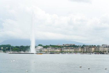 Cenevre 'nin ortasında, üzerinde bulutlu bir gökyüzü olan büyük bir çeşme vardır. Su sakin ve şehir hareketlilikle dolup taşıyor.