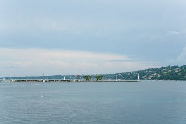 Cenevre 'nin ortasında, üzerinde bulutlu bir gökyüzü olan büyük bir çeşme vardır. Su sakin ve şehir hareketlilikle dolup taşıyor.
