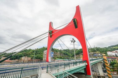 İspanya 'nın Bilbao kentindeki köprünün üzerinde kırmızı kemerli bir köprü görülüyor. Hava bulutlu ve bulutlu. Fotoğraf alçak bir açıdan çekilmiş..