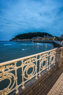 İspanya 'nın San Sebastian şehrindeki rıhtım, su ve dağ manzarası. Fotoğraf akşam geç saatlerde çekildi; gökyüzü koyu mavi ve çarpıcı..