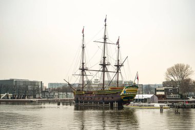 Hollanda 'nın Amsterdam şehrinde eski bir ahşap yelkenli gemi denizde duruyor. Fotoğraf bulutlu bir günde çekildi, gökyüzü bulutlu ve kasvetli. Gemi nakliye müzesinde sergileniyor..