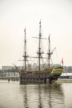 Hollanda 'nın Amsterdam şehrinde eski bir ahşap yelkenli gemi denizde duruyor. Fotoğraf bulutlu bir günde çekildi, gökyüzü bulutlu ve kasvetli. Gemi nakliye müzesinde sergileniyor..
