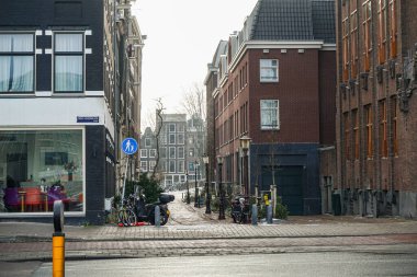 Amsterdam, Hollanda 'da bir sokak kavşağı. Sağ tarafta koyu tuğlalı binaların yanı sıra birçok sokak lambası, park edilmiş bisikletler ve motosikletler görülebiliyor. Fotoğraf bulutlu bir günde çekildi..