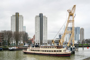 Hollanda 'daki Rotterdam Açık Hava Müzesi' nde büyük vinçli bir geminin arka planına karşı yüksek binalar. Hava bulutlu ve bulutlu..