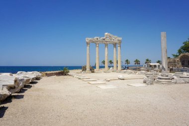 Çok sayıda sütun biçiminde antik bir Apollon Tapınağı ve Türkiye 'nin yanına gömülü bir kemer. Arka planda mavi Akdeniz var. Gökyüzü parlak ve mavi.