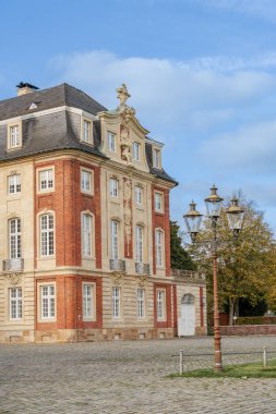Munster Almanya 'sında beyaz çatılı ve kırmızı tuğlalı ön cepheli büyük bir tuğla bina. Binanın bir sürü penceresi ve bir balkonu var. Sokaklar boş ve gökyüzü temiz.