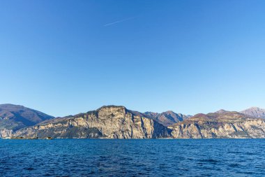İtalya 'da sakin mavi bir Garda Gölü ve suda bir tekne. Gökyüzü açık ve arkadaki dağlar karla kaplı..