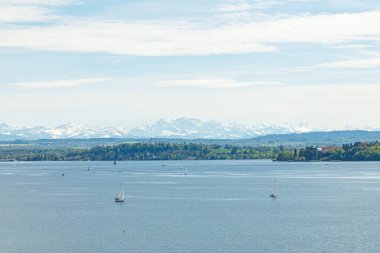 Alman tarafındaki Bodensee Gölü 'nde yüzen çok sayıda yelkenli vardı. Arka planda karla kaplı Alp dağlarından oluşan bir manzara var. Fotoğraf güneşli bir günde çekildi..