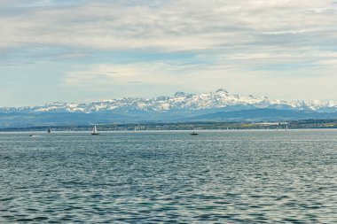 Alman tarafındaki Bodensee Gölü 'nde yüzen çok sayıda yelkenli vardı. Arka planda karla kaplı Alp dağlarından oluşan bir manzara var. Fotoğraf güneşli bir günde çekildi..