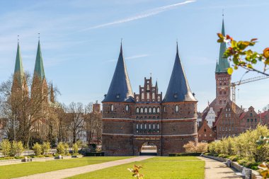 Lubeck, Almanya 'da Holstentor Müzesi' nin kurulması. Kenarları boyunca üç keskin kilise kulesi ve çeşitli binalar görülebilir durumda. Önümüzde yeşil çimenler var. Hava güneşli..