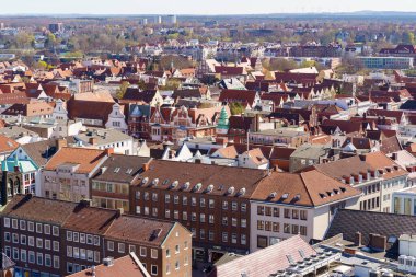 A city view with a river running through it in Lubeck Germany. The buildings are old and have red roofs. The city appears to be a mix of residential and commercial areas.