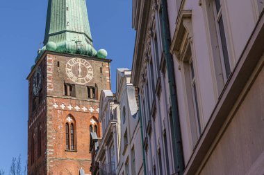 Almanya 'daki Lubeck şehrinin arka planında uzun yeşil bir çan kulesi var. Sokaklar ağaçlar ve binalarla dolu..