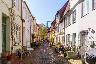 Lubeck Almanya 'sında dar bir kaldırım taşı caddesi. Arkasında bir sıra ev ve kilise var. Sokak saksı bitkileriyle ve açık hava oturma yerleriyle dolu, rahat ve davetkar bir atmosfer yaratıyor..