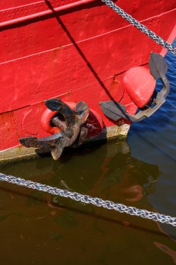 A red boat with a black anchor on it. The anchor is rusty and the boat is in the water