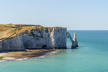 A beautiful blue ocean with a cliff in the background in Etretat France Normandy. The cliff is a part of a larger rock formation The shape of the stone arch resembles an elephant's trunk.