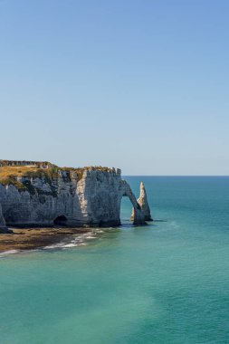 Etretat France Normandiya 'da arka planında bir uçurum olan güzel mavi bir okyanus. Uçurum, daha büyük bir kaya oluşumunun bir parçasıdır. Kaya kemerinin şekli bir filin gövdesine benzer..