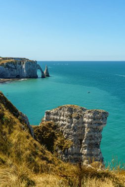 Fransa, Normandiya 'da, Etretat' ta okyanus suyunun zeminine karşı taştan kayaların ve kayaların harika manzarası var. Su ve gökyüzü mavi ve şeffaf. Hava açık..