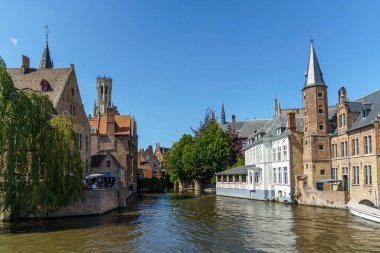 Bruges, Belçika 'daki bir kanaldan şehir manzarası. Sağda ve solda çeşitli kırmızı tuğla binalar görülebilir. Bruges Çan Çanı arka planda görünür..