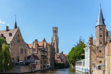 Bruges, Belçika 'daki bir kanaldan şehir manzarası. Sağda ve solda çeşitli kırmızı tuğla binalar görülebilir. Bruges Çan Çanı arka planda görünür..