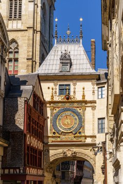 Fransa 'nın Rouen şehrinde tarihi astronomik saate sahip bir kule. Güneşli bir gün, arka planda sis görünüyor. Eski yarı ahşap evler görülebilir. Gökyüzü mavi ve berrak.