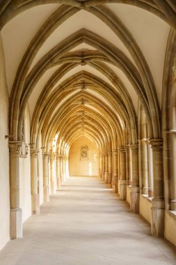 Gotik tarzında kemerli tavanları ve penceresi olan uzun, dar bir koridor. Kemerler kahverengi ve tavan beyaz..