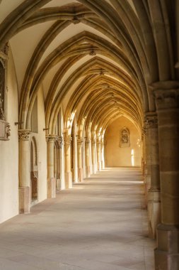 Gotik tarzında kemerli tavanları ve penceresi olan uzun, dar bir koridor. Kemerler kahverengi ve tavan beyaz..