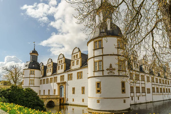 Paderborn Almanya 'sında Neuhaus Kalesi' nin önünde avlusu olan büyük beyaz bir bina. Avlu bir çakıl yolu ile çevrili ve bir sürü çiçek var..