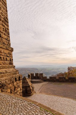 Büyük Wilhelm anıtından Almanya 'nın Port Westphalia kentinin manzarası. Ufukta bulutlu bir gökyüzü, akşam ve puslu tepeler var. Resim anıtın duvarlarını gösteriyor..